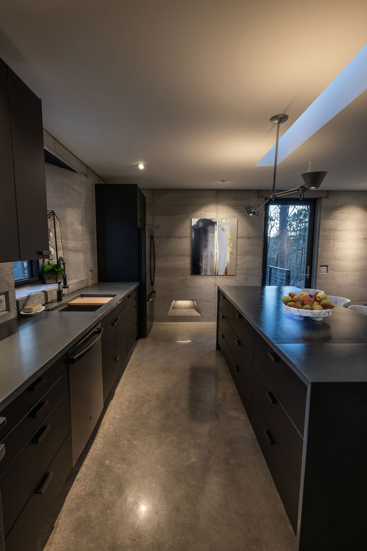 A modern kitchen in a rammed earth house featuring custom concrete countertops and matte black cabinets