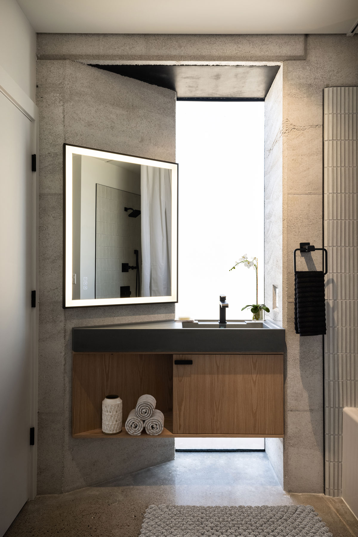 This floating custom concrete sink rests on a handcrafted modern oak cabinet in this rammed earth bathroom