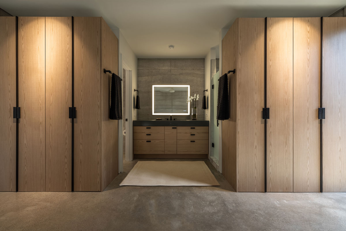 The bespoke oak wardrobes in the master bedroom frame the custom concrete sink set against a limestone rammed earth wall