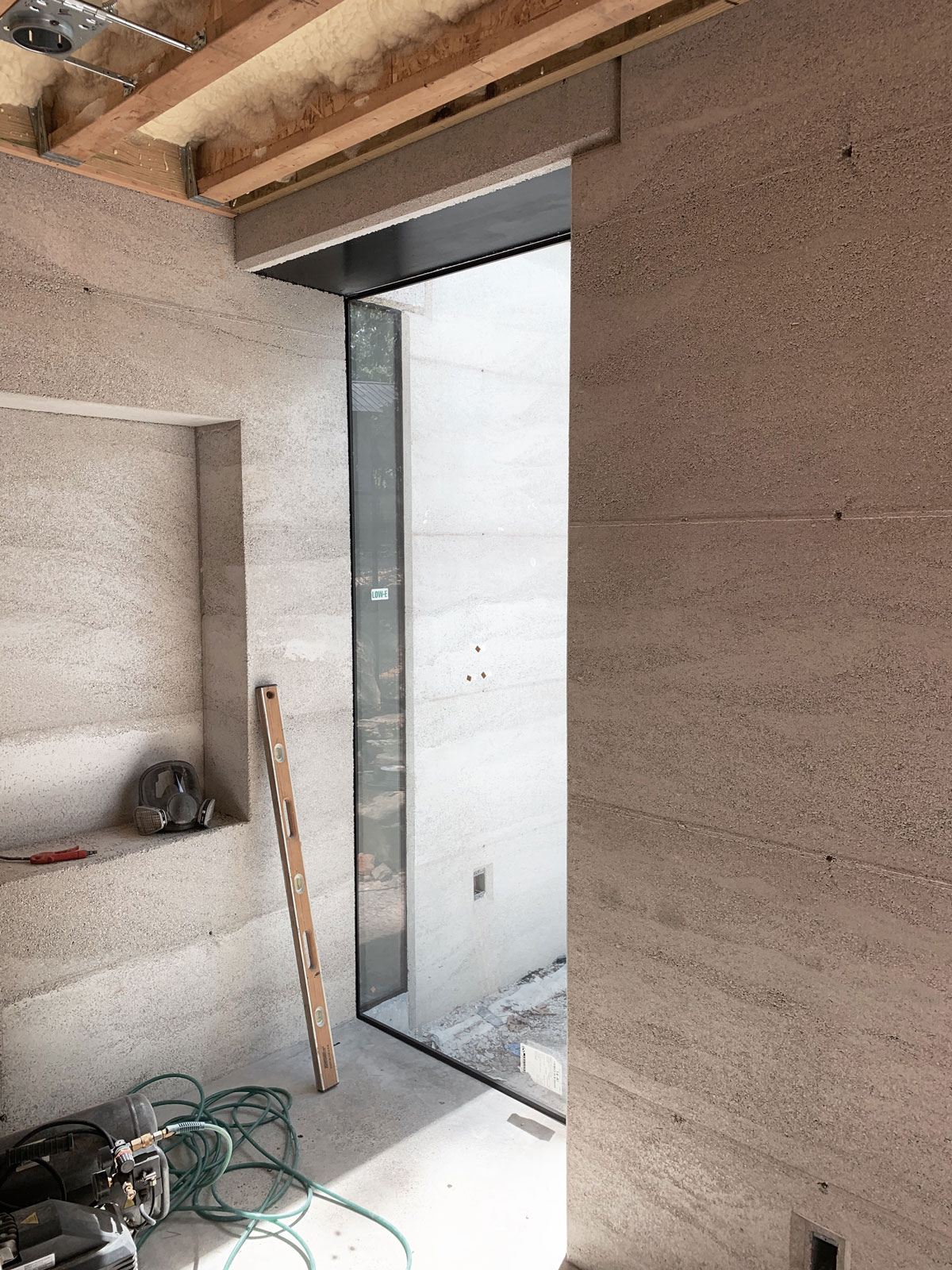 The corner window, integral bookshelf niche, spray foam, and lighting in the modern rammed earth house 