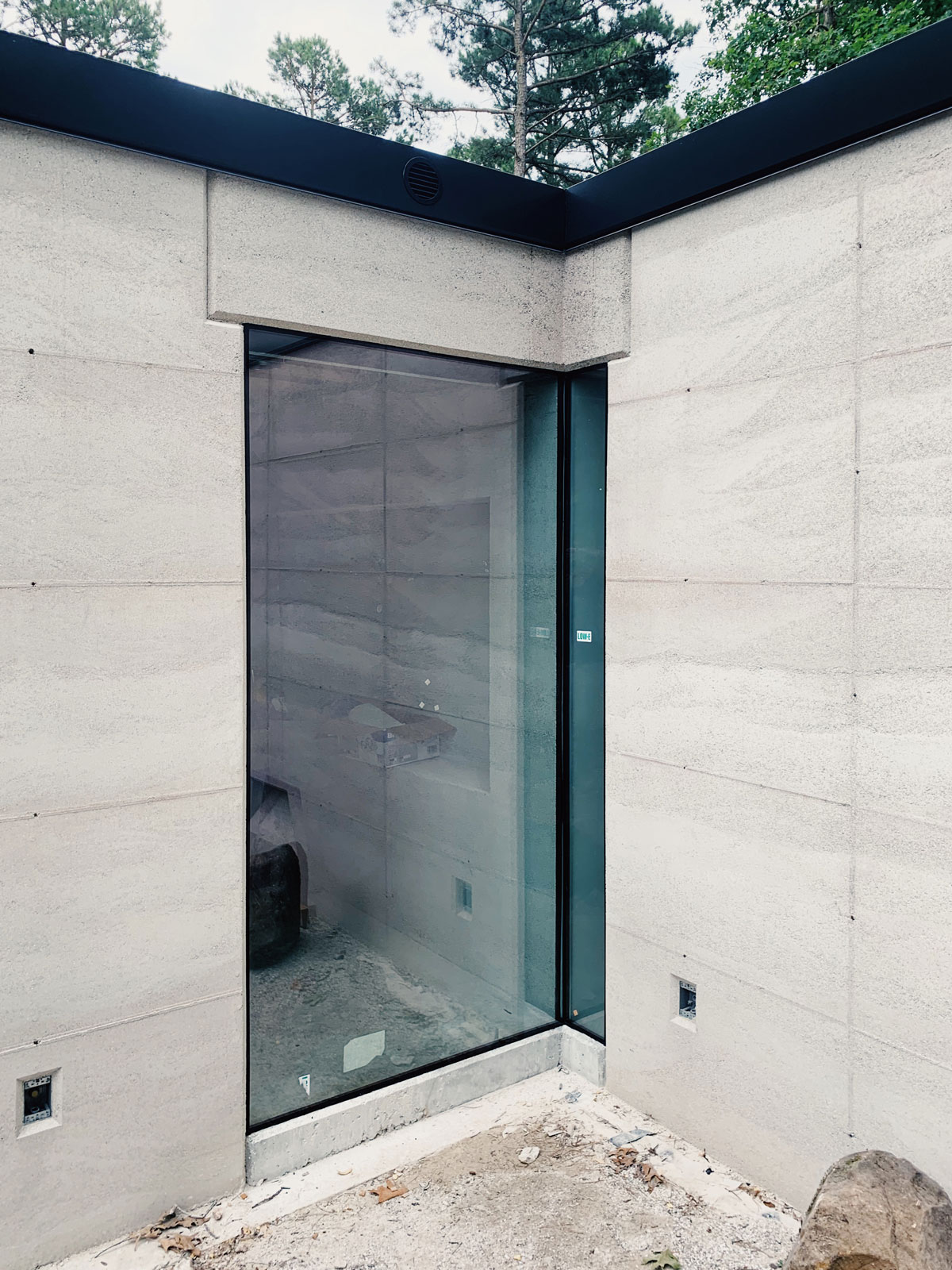 An intersection between two bedrooms where an L-shaped rammed earth lintel and a corner window meet